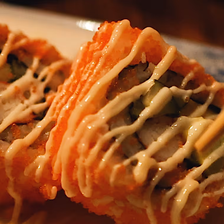 Close-up of sushi rolls topped with spicy mayo drizzle.